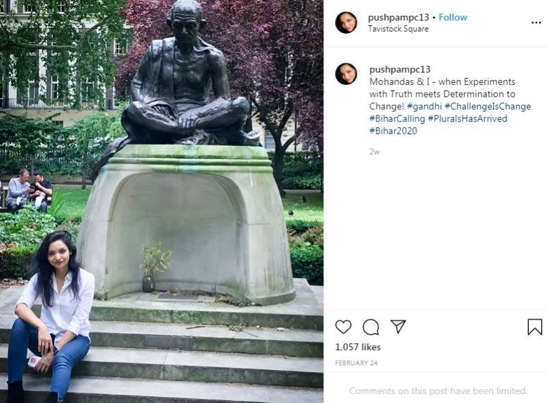 Pushpam Priya Choudhary sitting in front of a statue of Mahatma Gandhi