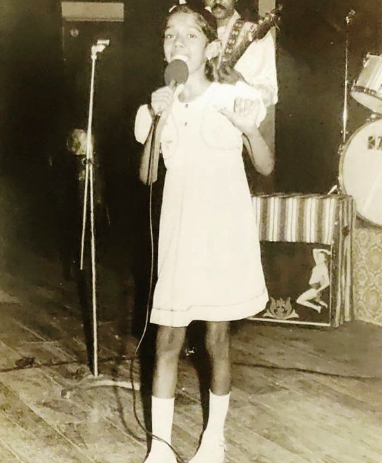 A childhood photo of Mahalakshmi Iyer singing in school