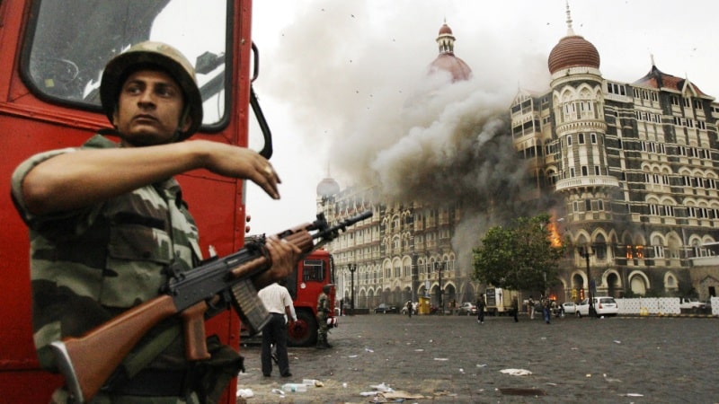 An Indian soldier taking cover behind a fire truck outside Taj Hotel during the 2008 Mumbai Attacks