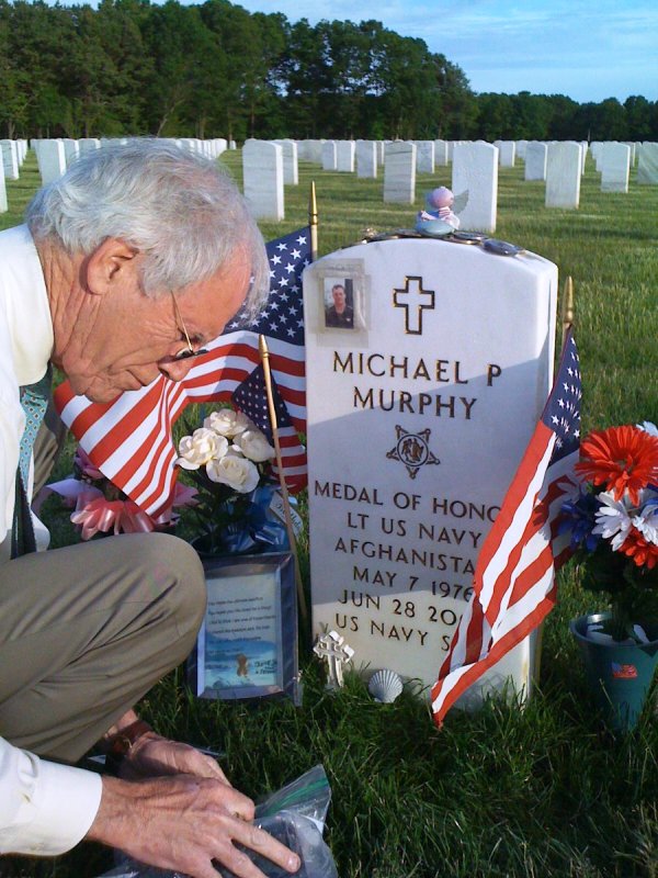 A photo of Dan Murphy sitting next to Michael's grave at the Calverton National Cemetery
