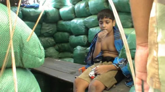 Balachandran Prabhakaran in custody of Sri Lankan Army with a snack in his hand while sitting on a bench surrounded by sandbags in a fortified army position