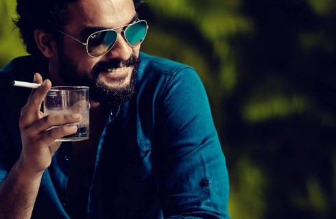 Tovino Thomas while smoking a cigarette and drinking an alcoholic beverage