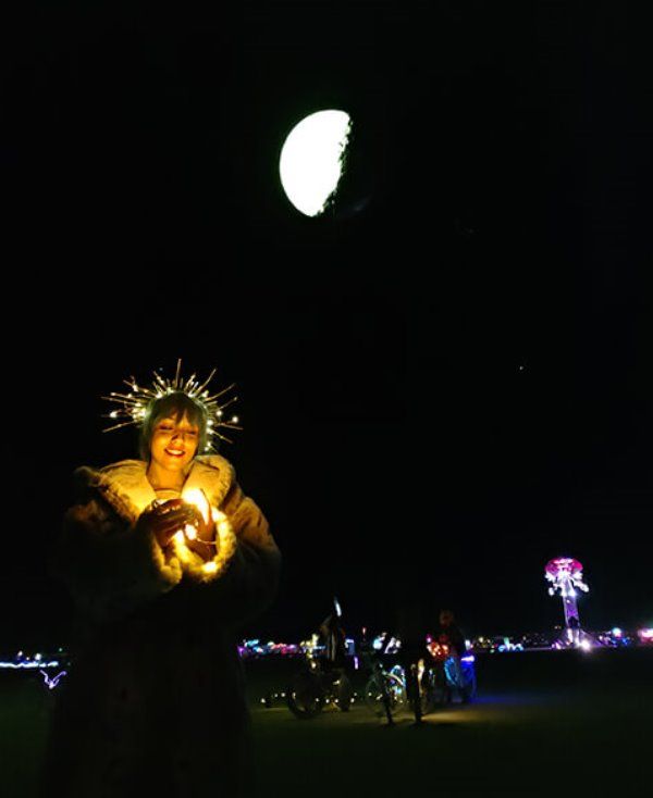 Lekha Washington with her artwork 'Moondancer' (at the background) at Burning Man Festival 2018